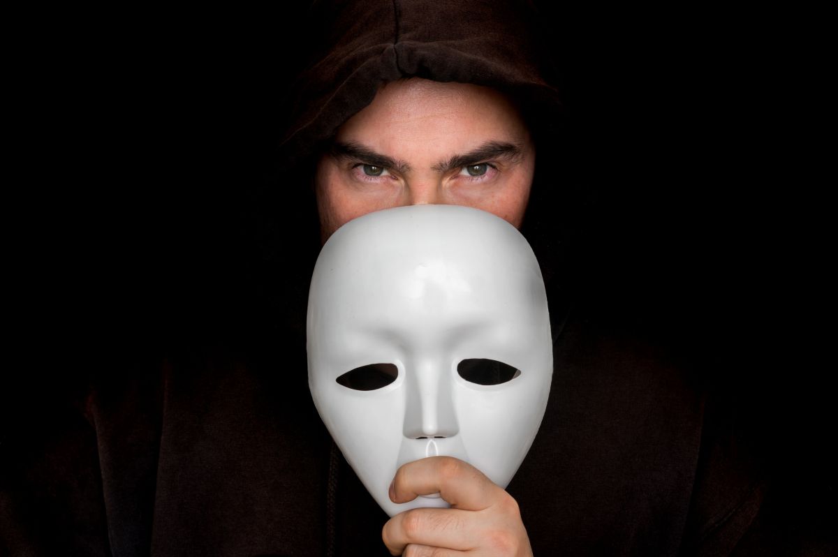 Mysterious man in black hiding his face behind white mask - anonymous concept. Bild: © istock.com / andriano_cz