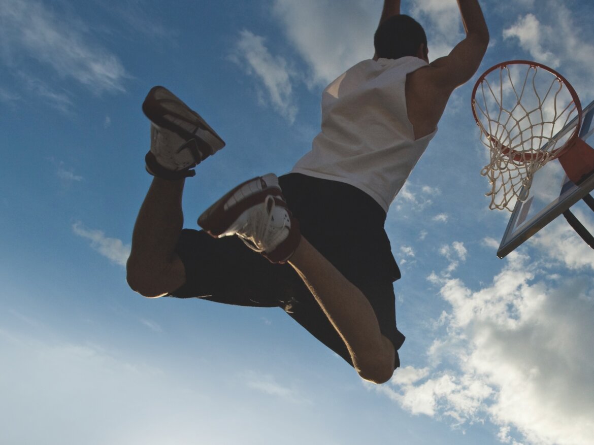 Mann springt mit Basketball zum Korb und versenkt den Ball.