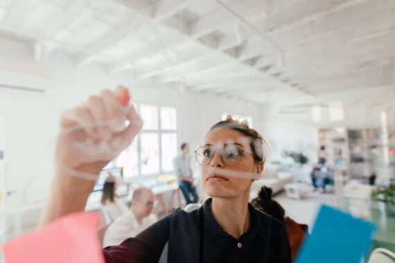 Lünendonk 2022: Unternehmen stemmen digitale Transformation. Eine Frau schreibt an ein transparentes Wipe-Board. Bild: © AleksandarNakic / Getty Images