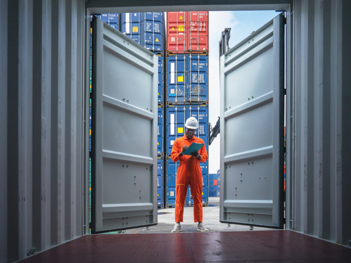 Logistik / Import / Export: Container auf einem Frachtschiff werden von einem Arbeiter kontrolliert