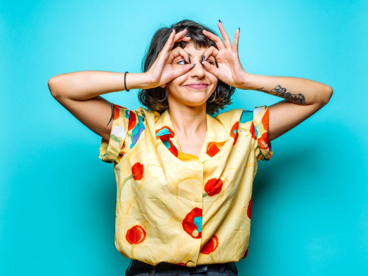Witziges Bild: Junge Frau mit gelb-bunter Bluse formt mit ihren Fingern Brillengläser. q.beyond Symbolbild für Microsoft Inspire 2023